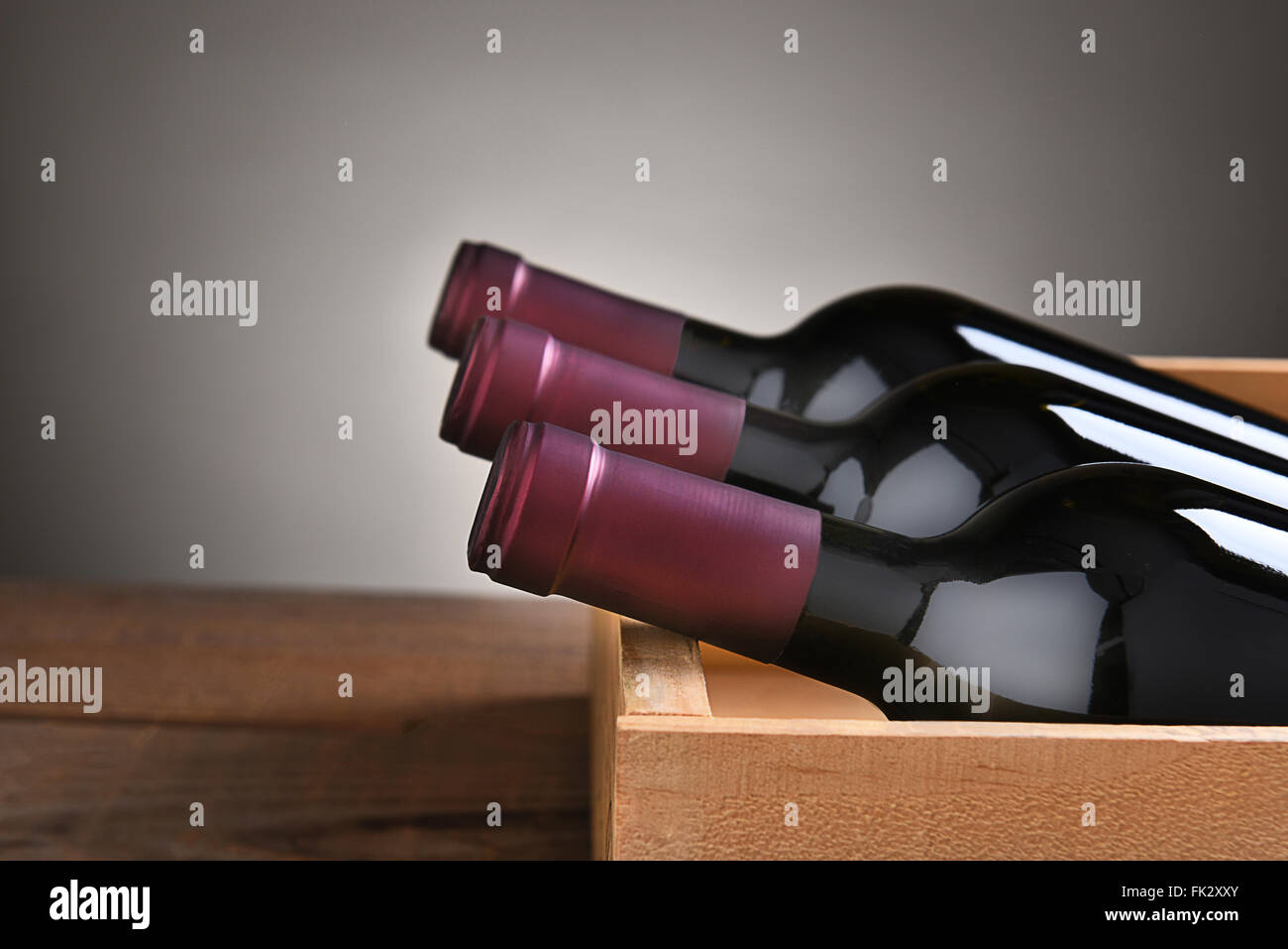 Drei Flaschen Rotwein in einer hölzernen Kiste mit einer leichten bis dunkelgrauen Hintergrund. Stockfoto