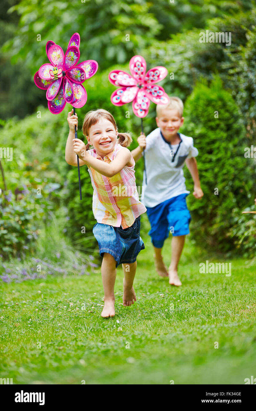 Zwei glückliche Kinder, die laufen im Garten im Sommer mit Windmühlen Stockfoto