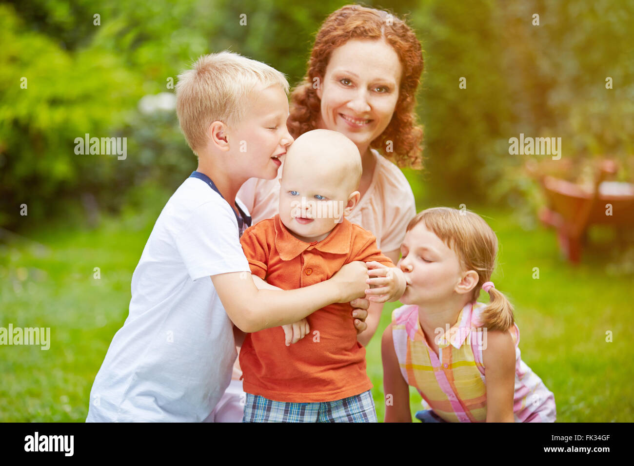 Familie mit Baby und zwei Kinder zusammen in einem Garten im Sommer Stockfoto
