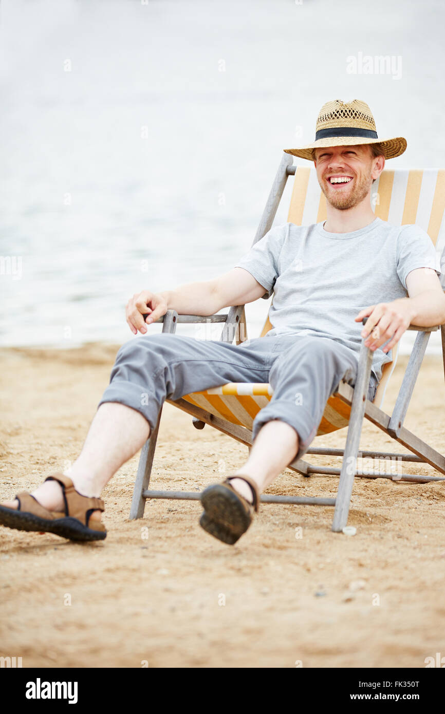Glücklicher Mann sitzt entspannt im Liegestuhl am Strand im Sommer Stockfoto