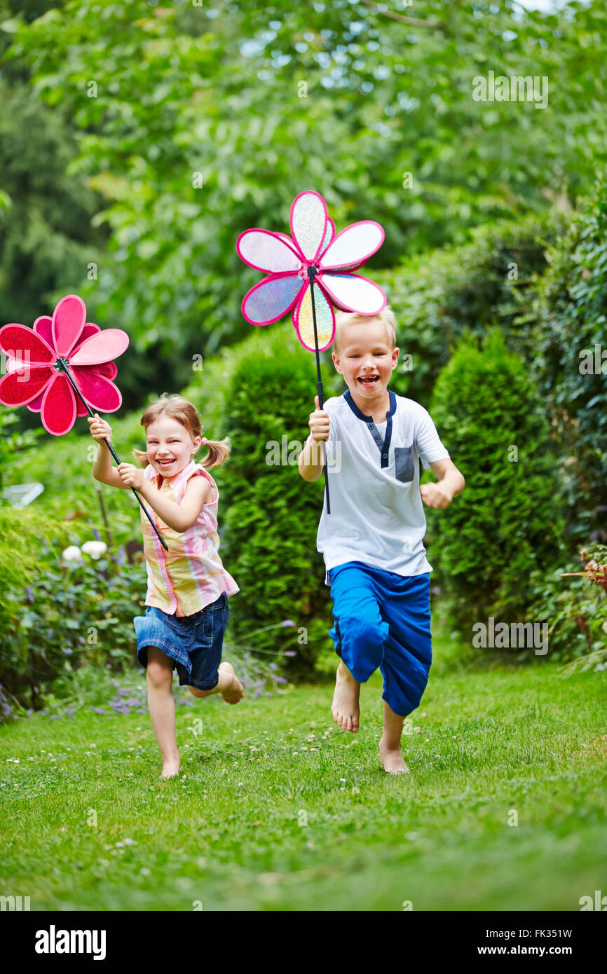 Zwei glückliche Kinder, die laufen mit Windmühlen im Garten im Sommer Stockfoto