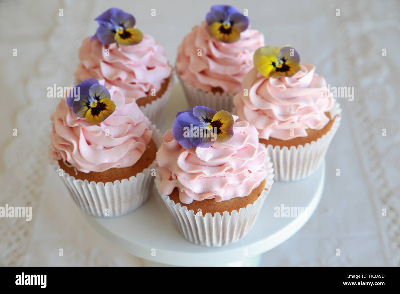 Hausgemachte rosa Zuckerguss Vanille Cupcakes mit essbaren Blüten Stockfoto