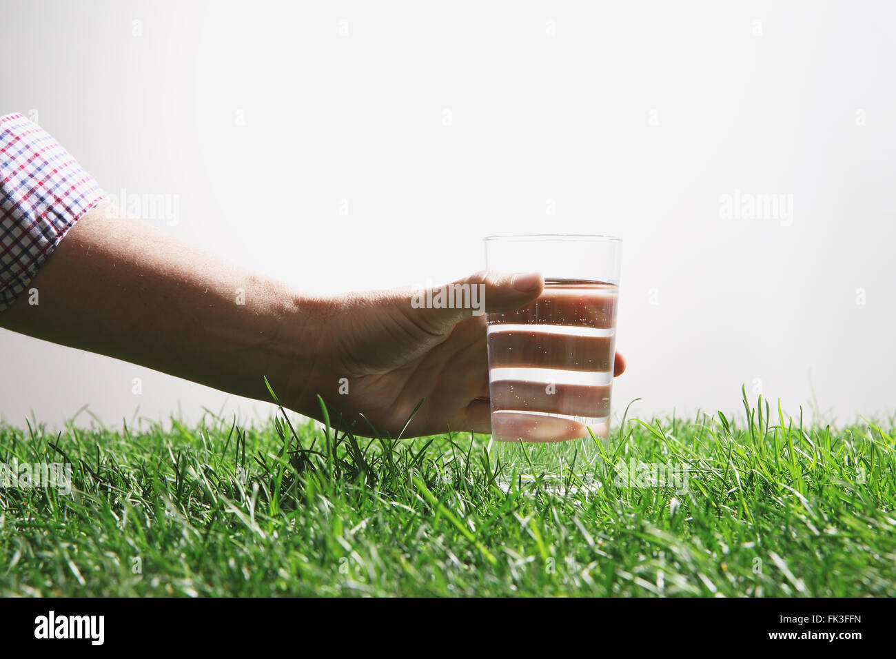 Hand, die Kommissionierung Glas Wasser auf dem Rasen Stockfoto