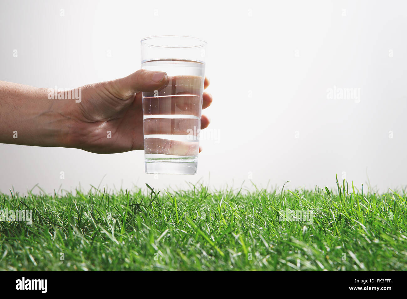 Hand, die Kommissionierung Glas Wasser auf dem Rasen Stockfoto