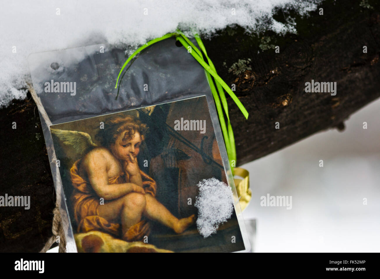 nachdenklicher Engel, Detail der klassischen Malerei zeigt einen Engel, ausgeschnitten und in Kunststoff-Abdeckung gebunden an einen Baum, mit Schnee bedeckt Stockfoto