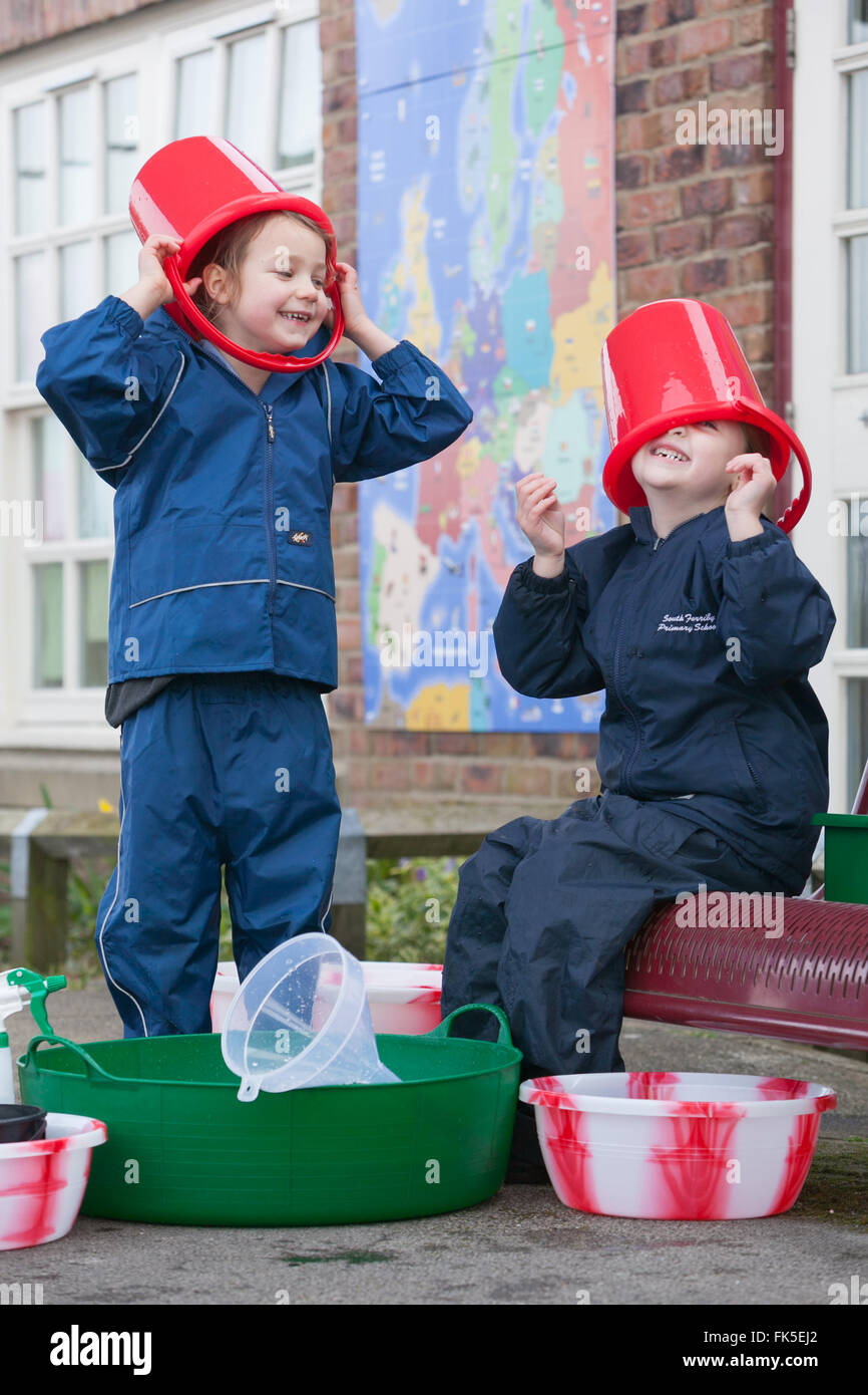Draußen mit verschiedenen Eimer und Spielzeug spielen zwei Grundschüler Wasser genießen. Stockfoto