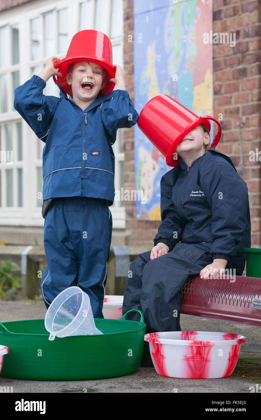 Draußen mit verschiedenen Eimer und Spielzeug spielen zwei Grundschüler Wasser genießen. Stockfoto