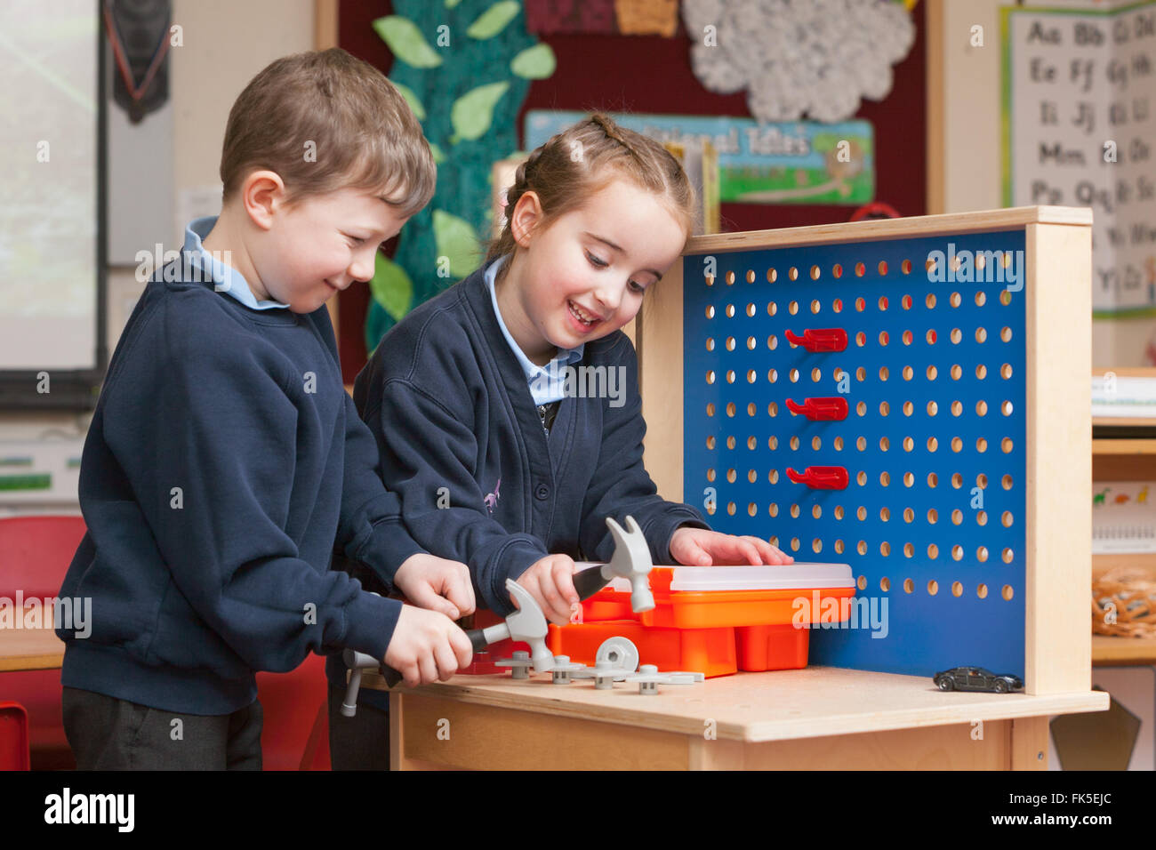 Schülerinnen und Schüler in Schuluniform in einer Grundschule im Vereinigten Königreich mit Spielzeug spielen Handwerkzeuge. Stockfoto