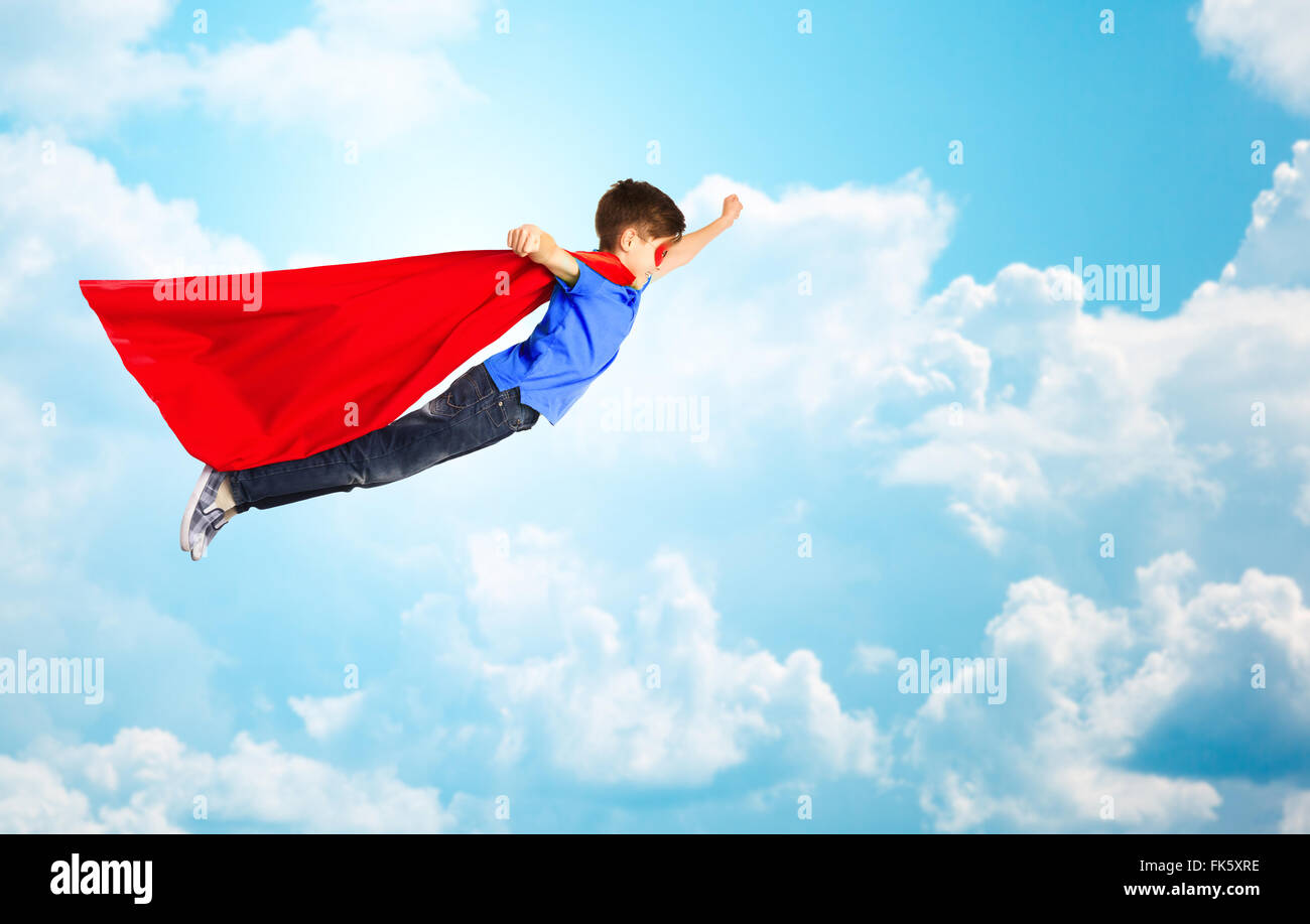 Junge im roten Superhelden Cape und Maske, die über den Himmel fliegen Stockfoto