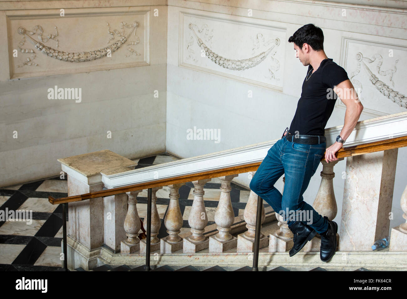 Seitenansicht des jungen dunkelhaarigen Mann hinunter auf Geländer im Museum. Weiße Wände mit Ornament verziert. Stockfoto