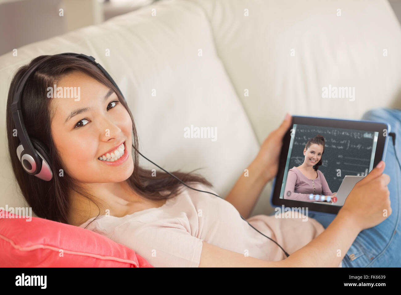 Zusammengesetztes Bild eines Mädchens mit ihrem TabletPC auf dem Sofa und Musikhören lächelnd in die Kamera Stockfoto