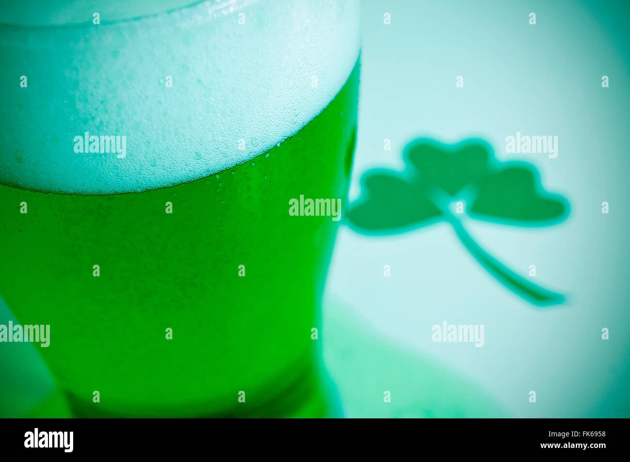 Nahaufnahme eines Glases mit gefärbten Jungbier und eine dreiblättrige Kleeblatt im Hintergrund, zum St. Patricks day Stockfoto