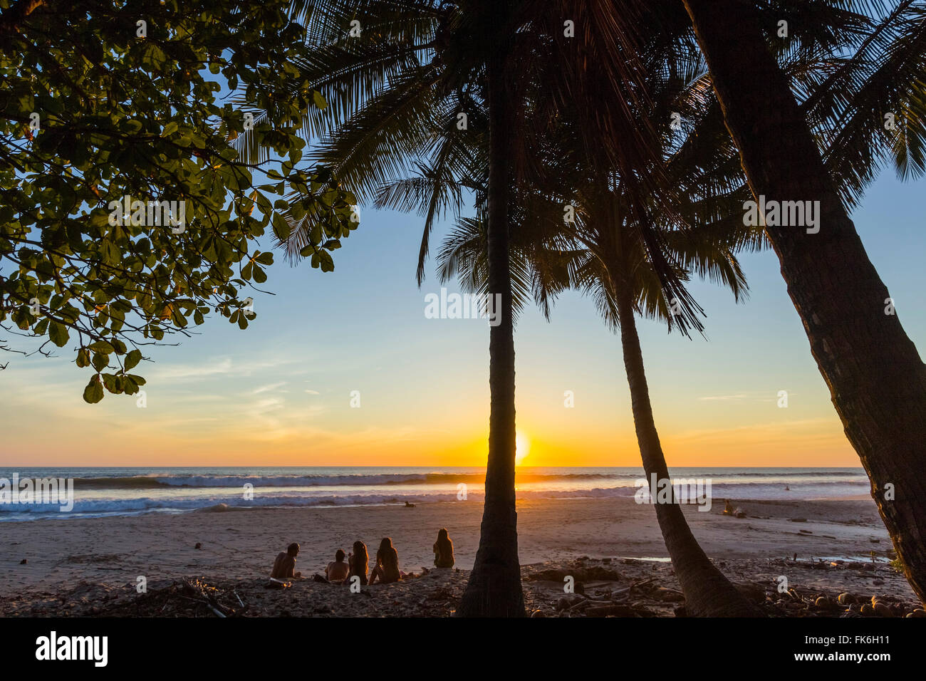 Menschen, die von Palmen bei Sonnenuntergang am Strand von Playa Hermosa, weit südlich der Halbinsel Nicoya, Santa Teresa, Puntarenas, Costa Rica Stockfoto