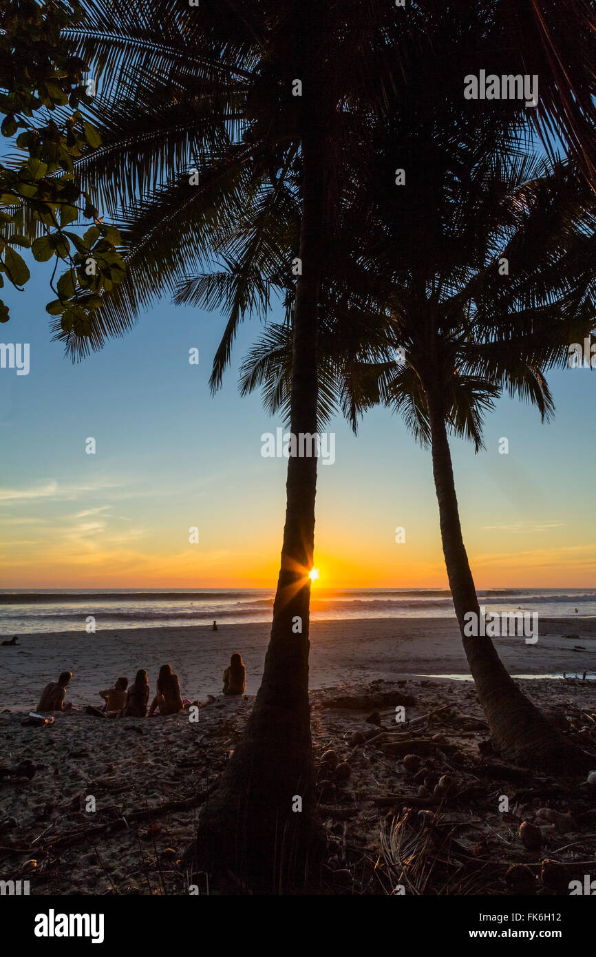 Menschen, die von Palmen bei Sonnenuntergang am Strand von Playa Hermosa, weit südlich der Halbinsel Nicoya, Santa Teresa, Puntarenas, Costa Rica Stockfoto