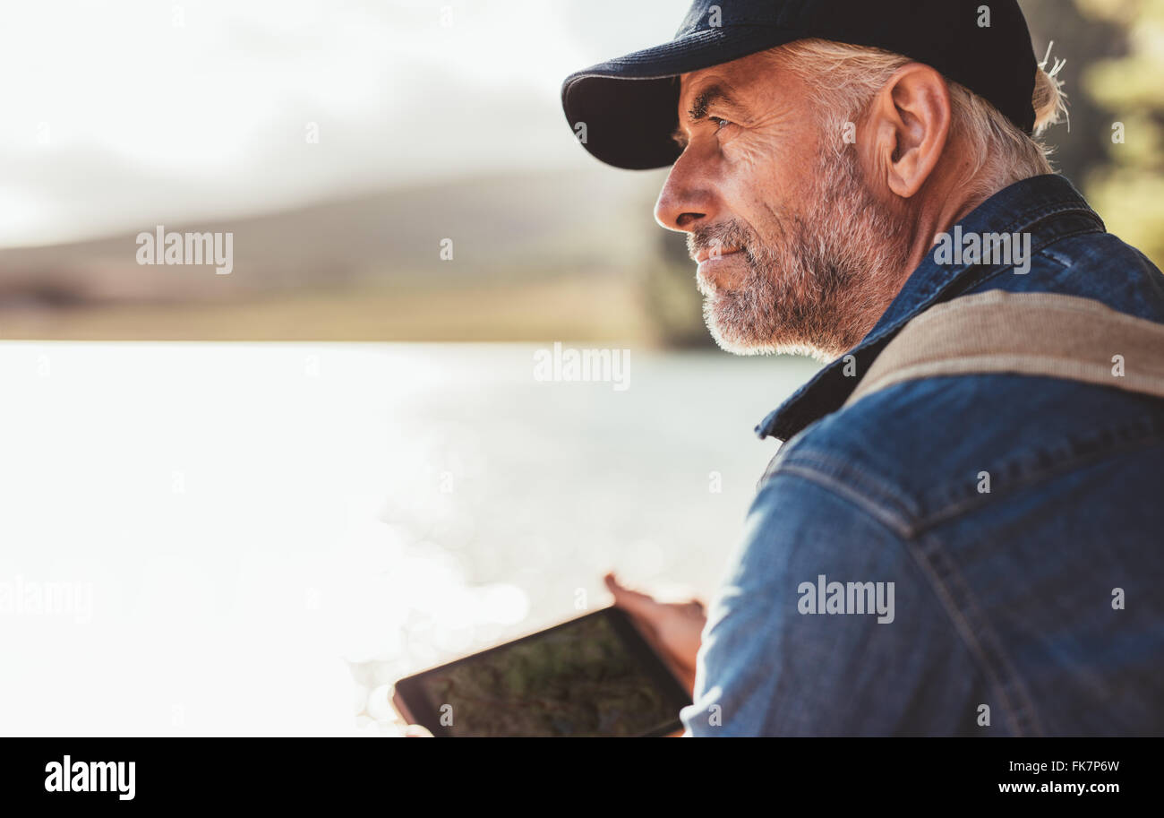 Nahaufnahme Portrait von reifer Mann mit Mütze sitzt an einem See und Blick auf einen Blick. Senior kaukasischen Mann mit Bart. Stockfoto