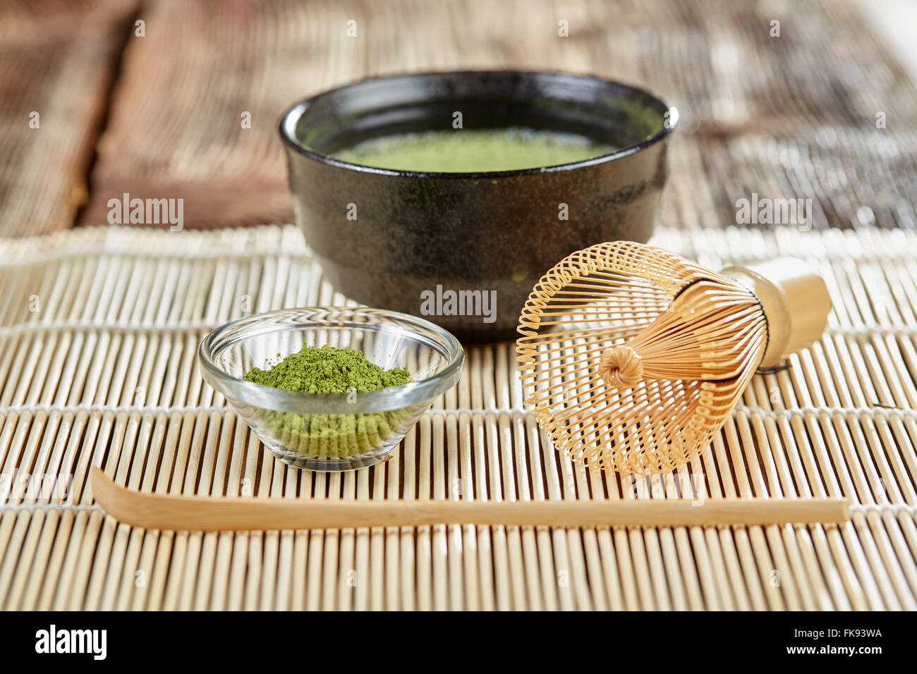 Grünen Matcha Teezubereitung mit Glasschale Schüssel, Schneebesen, Löffel und Tee auf einer Bambusmatte Tabelle Stockfoto