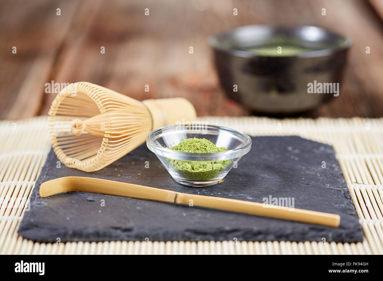 Grünen Matcha-Pulver, Tee und Schneebesen und Löffel für die Vorbereitung auf schwarzen Steinplatte und weißen Tisch Bambusmatte Stockfoto