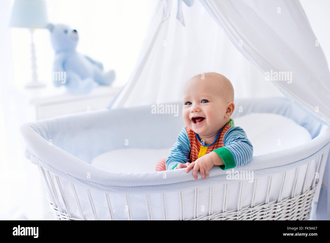 Lustige Baby in weißes Kinderbett mit Baldachin. Kindergarten Interieur und Bettwäsche für Kinder. Kleiner Junge spielt im Körbchen lachen Stockfoto