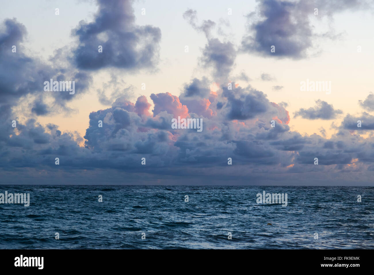 Flauschige Wolken schwebend über turbulente Meerwasser direkt am Sandstrand. Stockfoto