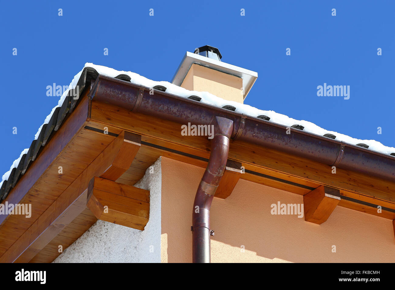 Neues Dach Top Detail mit Keramikfliesen, Schornstein und Kupfer Wasserrinne mit Schnee gegen blauen Himmel Stockfoto