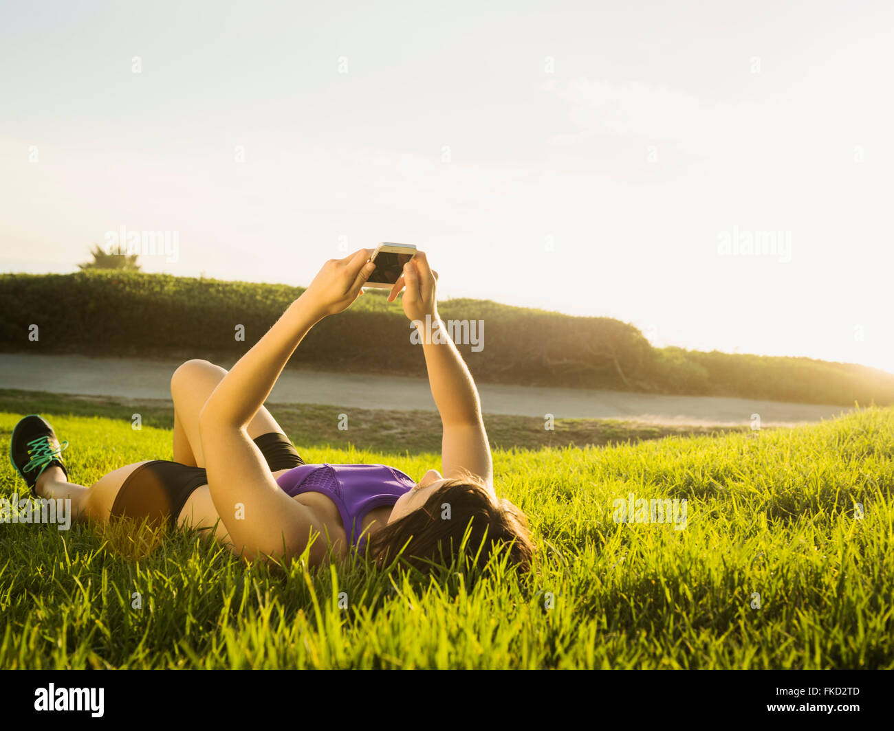Junge Frau liegt auf dem Rasen mit Telefon Stockfoto