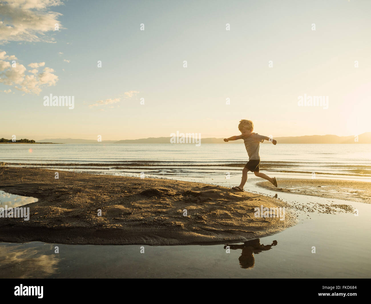 Kleiner Junge (4-5) an sonnigen Tag über Wasser springen Stockfoto