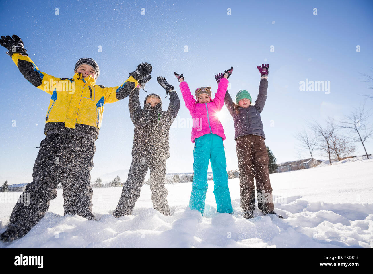 Kinder (8-9, 10-11) stehen im Schnee mit erhobenen Armen Stockfoto