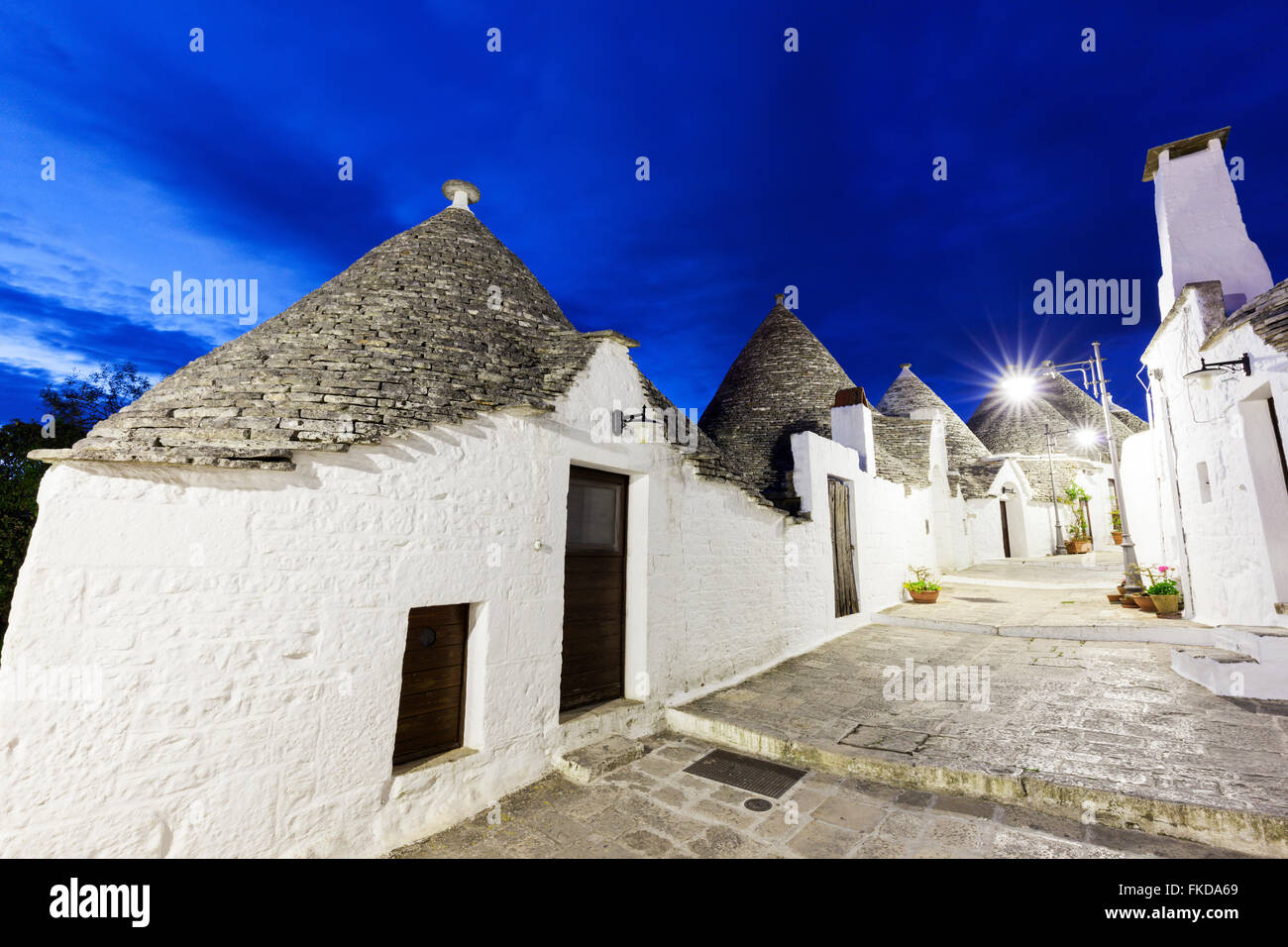 Trulli Häuser entlang der beleuchteten Street unter blauem Himmel Stockfoto