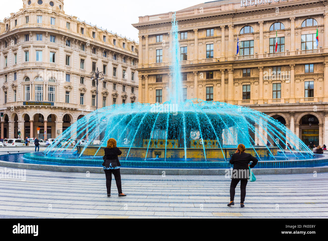Zwei Frauen sehen erstaunt die Brunnen mit blauem Wasser (gefärbt, um die Messe zu feiern) in Piazza de Ferrari Genua, Italien Stockfoto