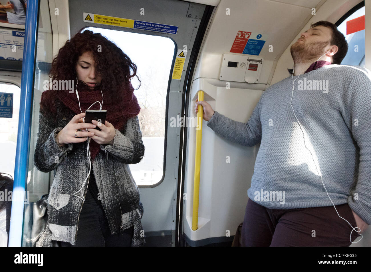 Ein junger Mann und eine Frau in einem Londoner u-Bahn Zug anhören von Musik auf ihrem Handy, London UK Stockfoto