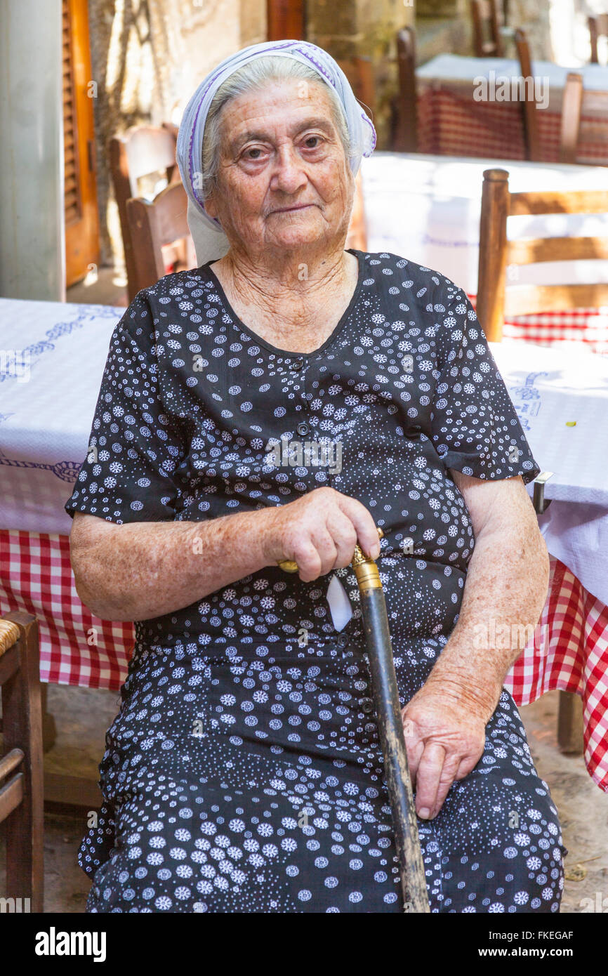 Ältere Frau sitzt, hält einen Spazierstock, im Dorf Mesta, Chios, Griechenland Stockfoto