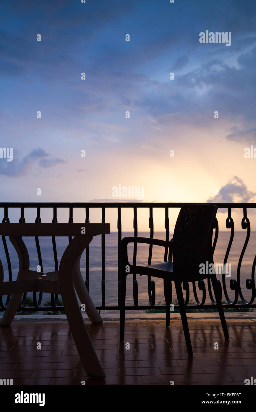Sessel und Tisch stehen auf dem Balkon. Meerblick über helle Sonnenaufgang Himmel Stockfoto