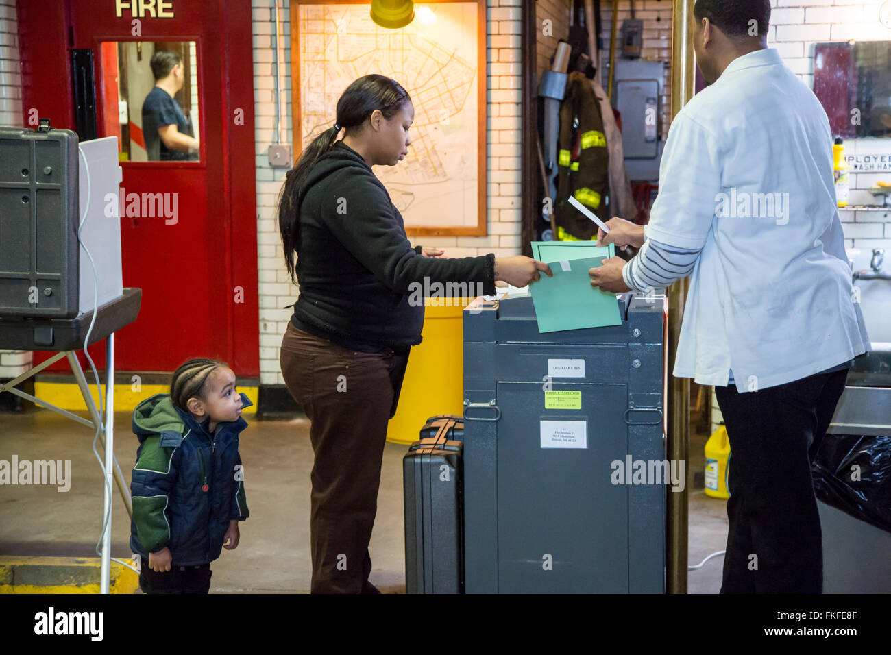 Detroit, Michigan, USA. 8. März 2016. Beamter (rechts) Wahl hilft ein Wähler ihre Stimmzettel durch einen elektronischen Stimmenauszählung Maschine Detroits Feuerwache # 3 als ihr Kind Uhren laufen. Sie wurde in primären Präsidentschaftswahl Michigans abstimmen. Bildnachweis: Jim West/Alamy Live-Nachrichten Stockfoto