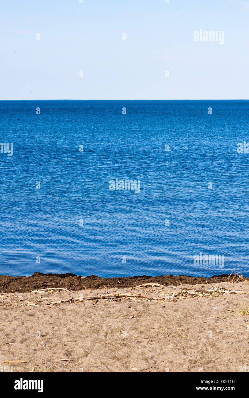 Der Strand am blauen Wasser, das gegen die weissen Himmel. Stockfoto