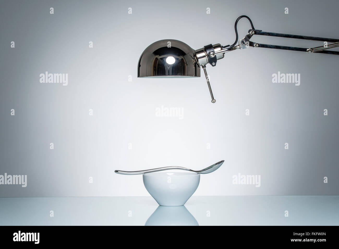 leuchten weiße Keramikschale Silberlöffel mit Schreibtischlampe auf Runde Studiobeleuchtung Stockfoto