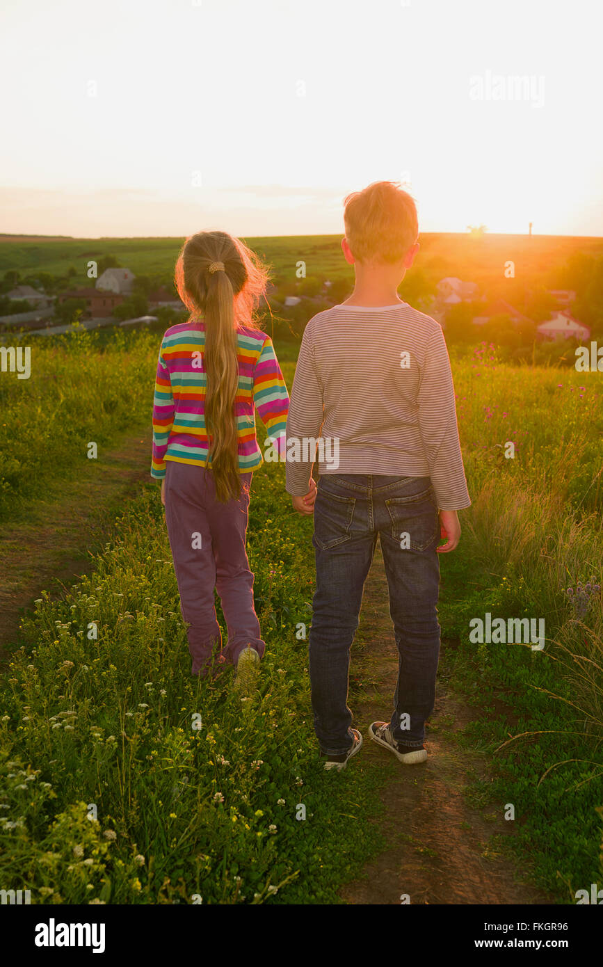 Jungen und Mädchen Hand in Hand und zu Fuß entlang der Straße bei Sonnenuntergang Stockfoto