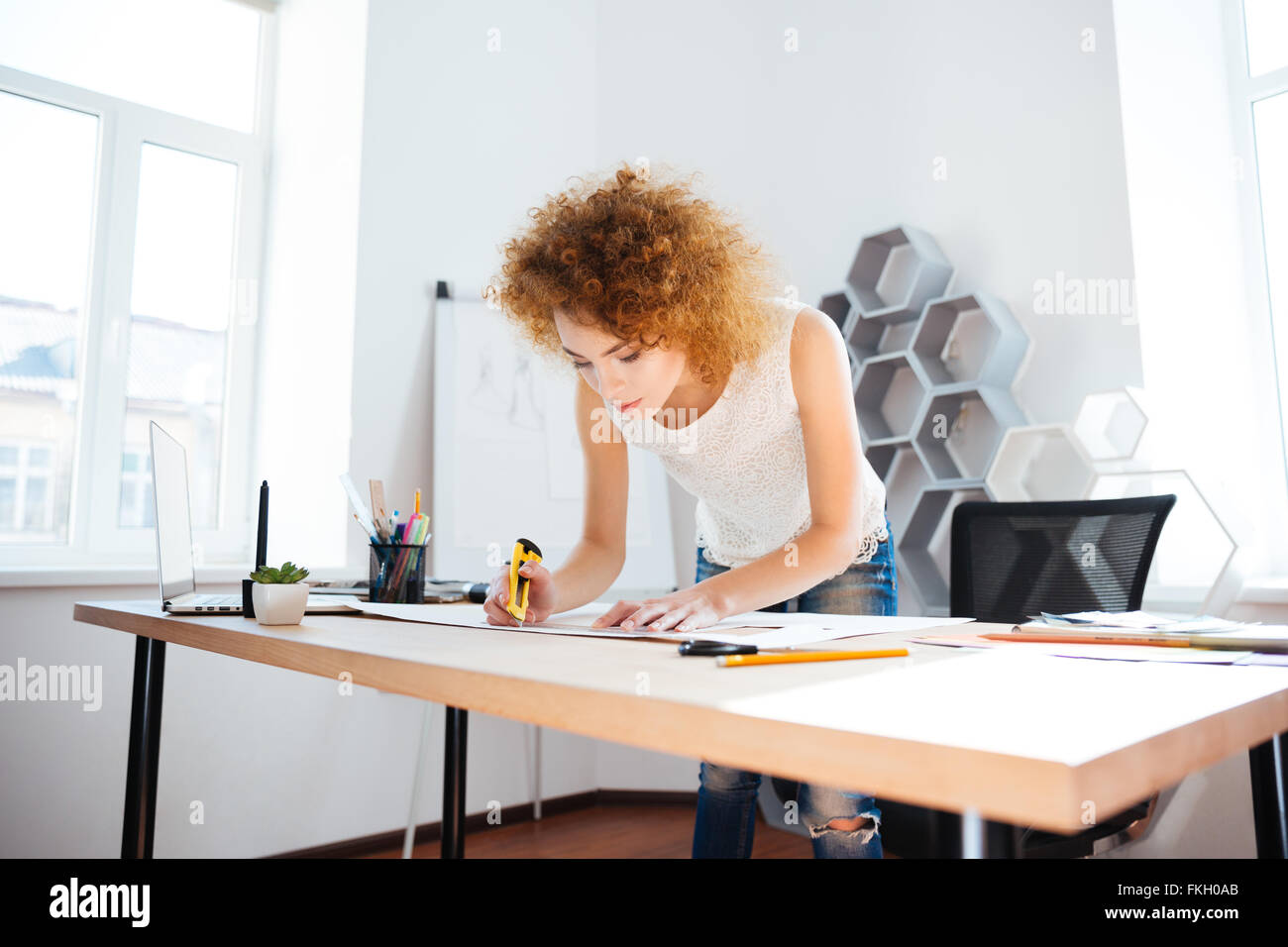 Fotograf Ernst attraktive junge Frau mit lockigen roten Haaren arbeitet im Büro mit Briefpapier Messer Stockfoto