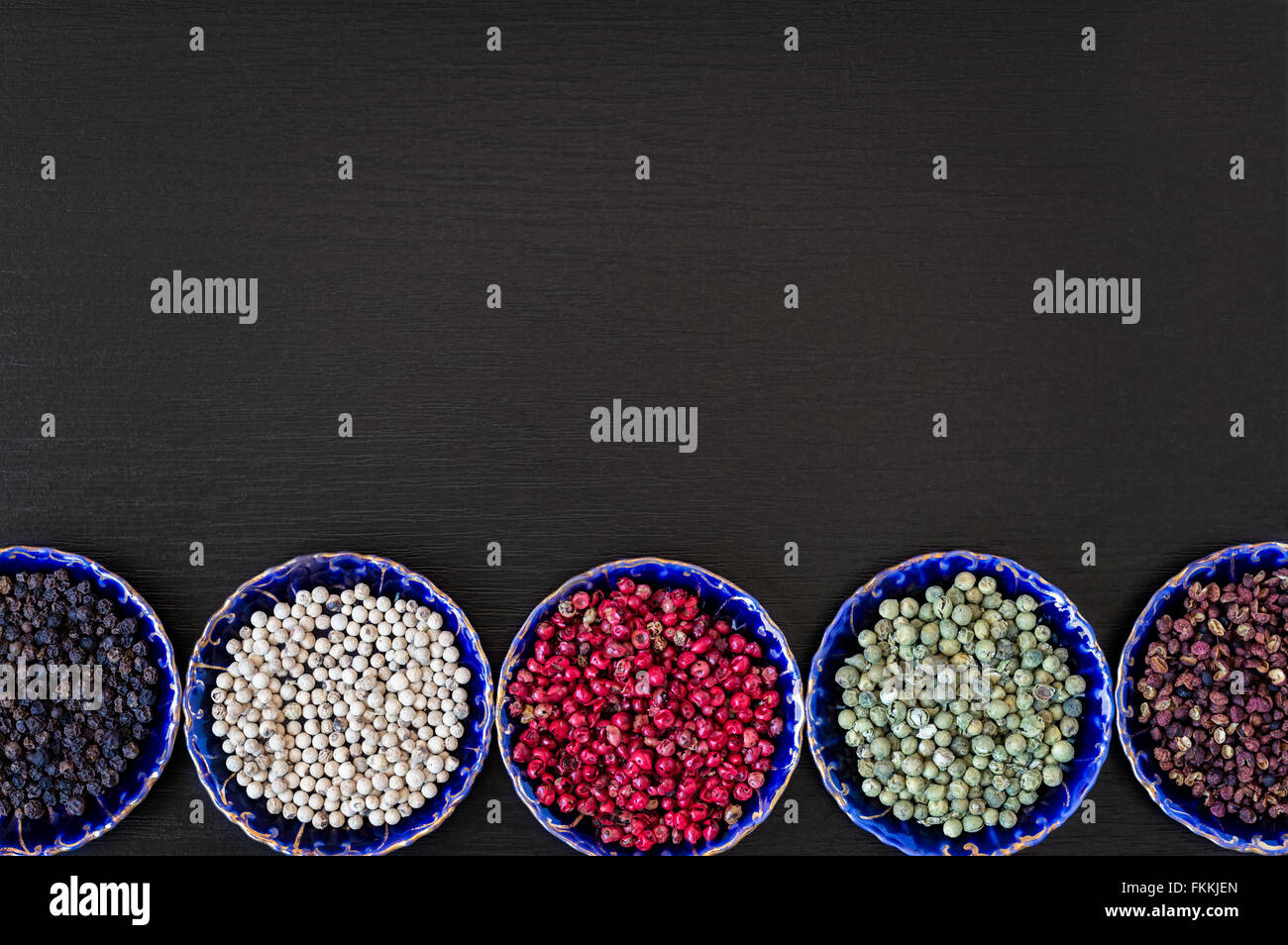 Sichuan, weiße, rote, grüne und schwarze Pfefferkörner in blau Vintage Keramik Untertassen auf einem schwarzen Holztisch. Stockfoto