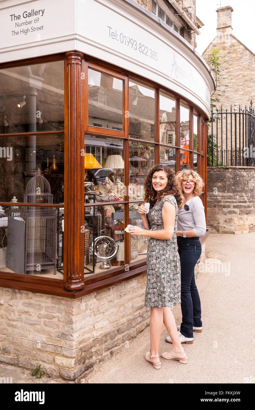 2 Frauen reinigen das Schaufenster der Galerie Shop Shop in Burford, Oxfordshire, England, Großbritannien, U Stockfoto