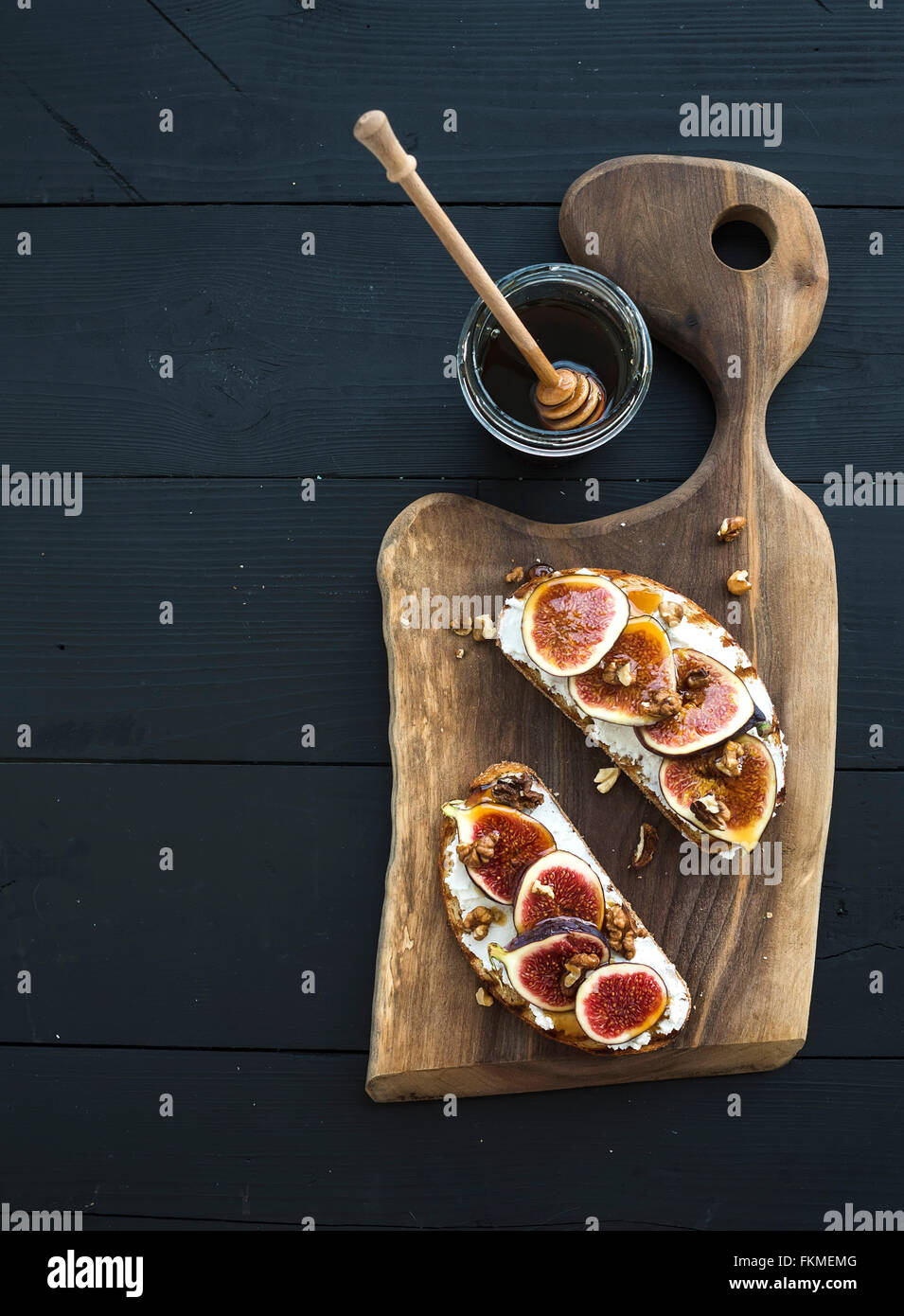 Sandwiches mit Ricotta, frische Feigen, Walnüssen und Honig auf rustikalem Holzbrett auf schwarzem Hintergrund, Ansicht von oben Stockfoto