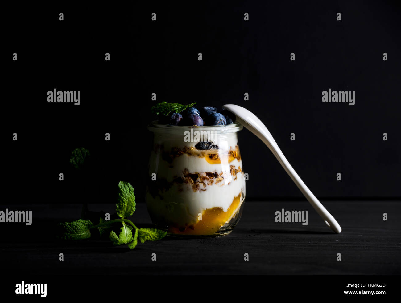 Joghurt und Hafer-Müsli mit Marmelade, Blaubeeren und Minze Blätter in Glas auf schwarzem Hintergrund, selektiven Fokus Stockfoto
