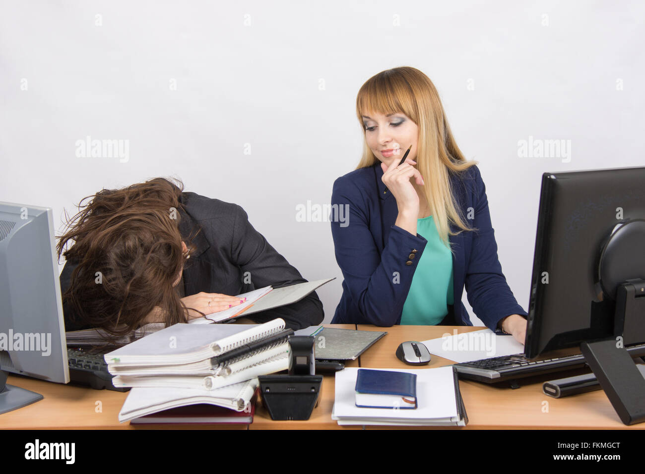 Weiblichen Kollegen im Büro, eine eingeschlafen auf einen Haufen von Ordnern, die zweite mit einem Grinsen schaut sie an Stockfoto