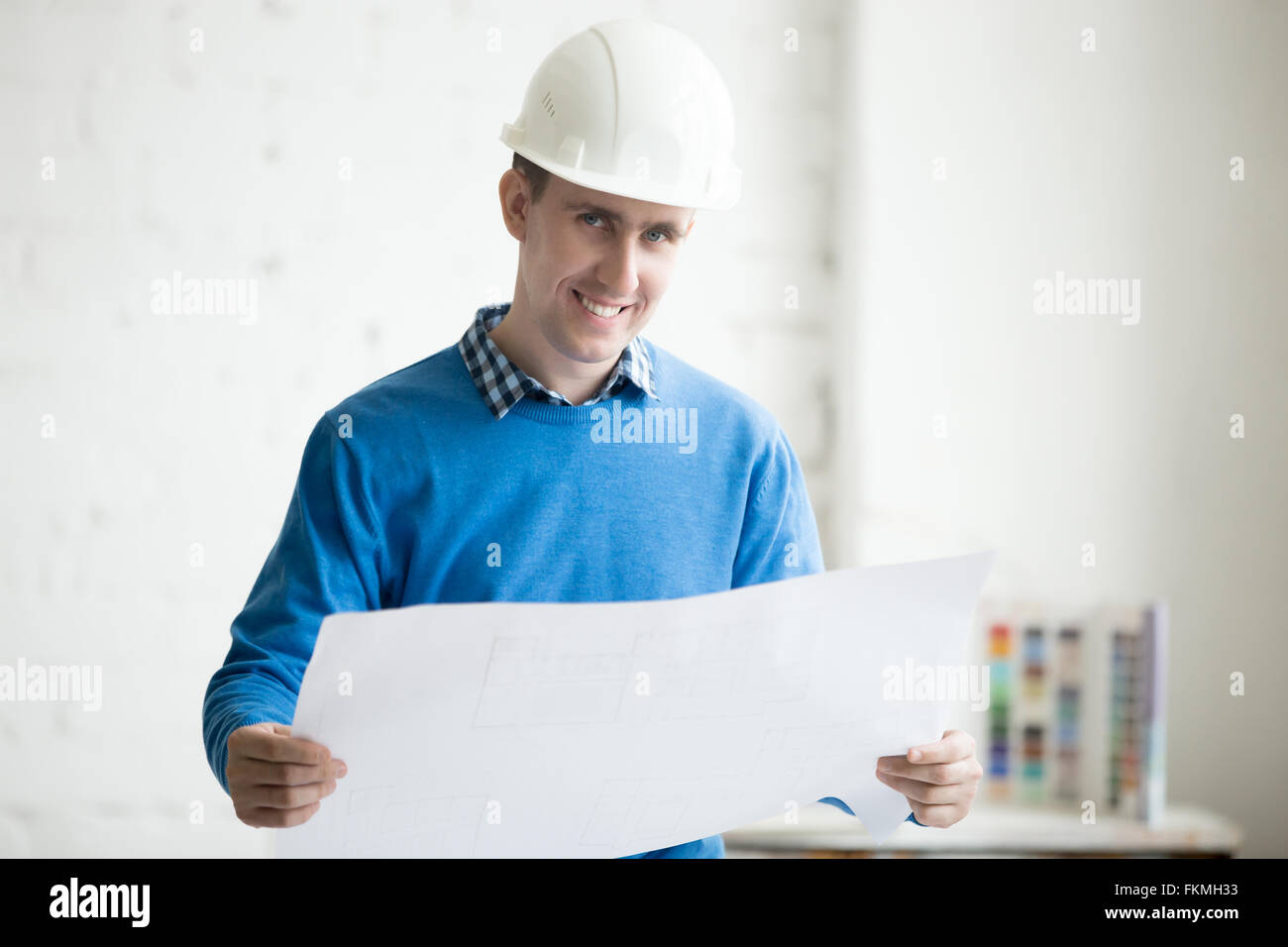 Porträt der junge fröhlich schön Ingenieur in weißen Helm holding Blaupause, stehend im architektonischen Agentur Büro Stockfoto