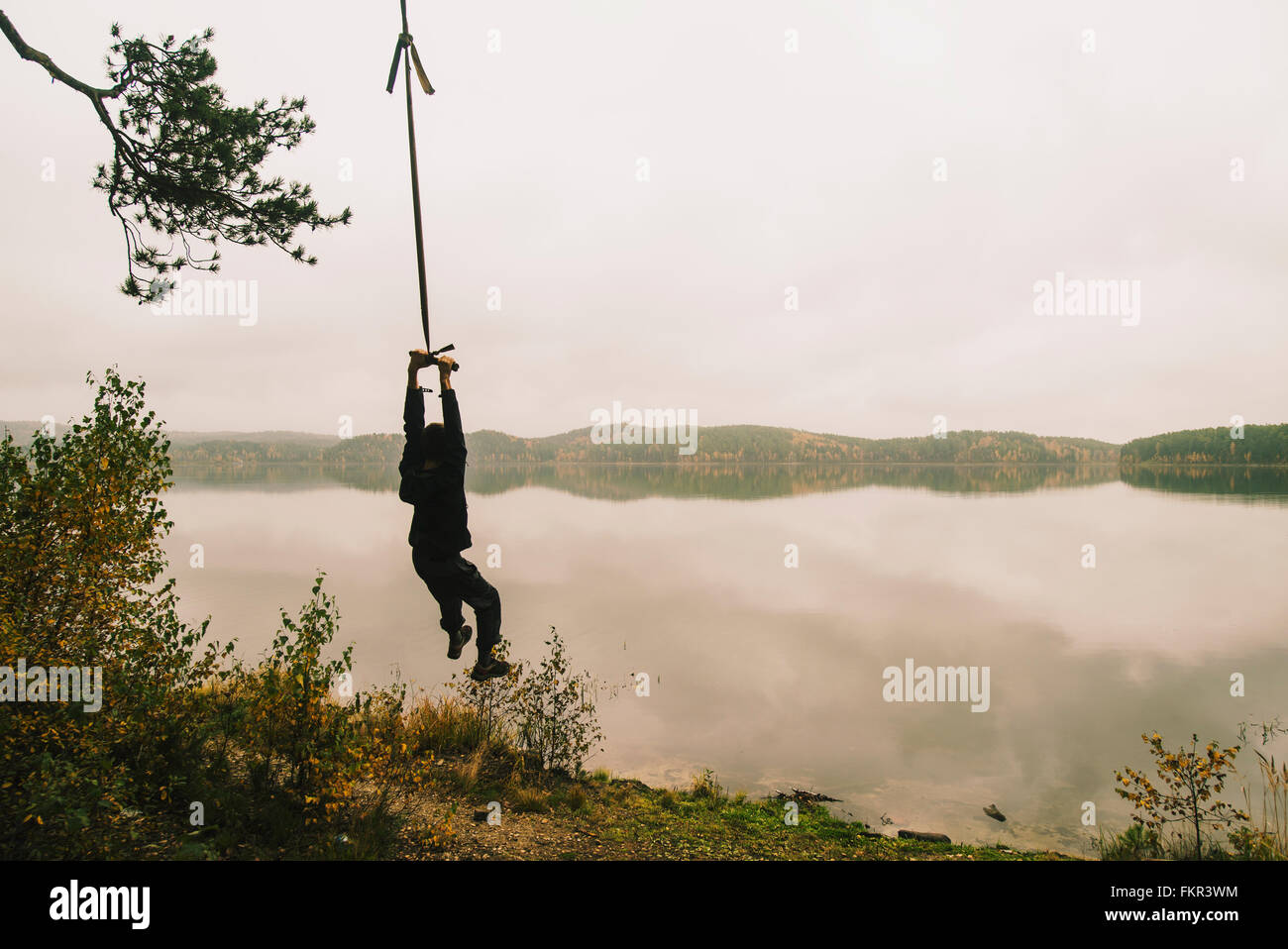 Mann hängen am Seil schwingen am abgelegenen See Stockfoto