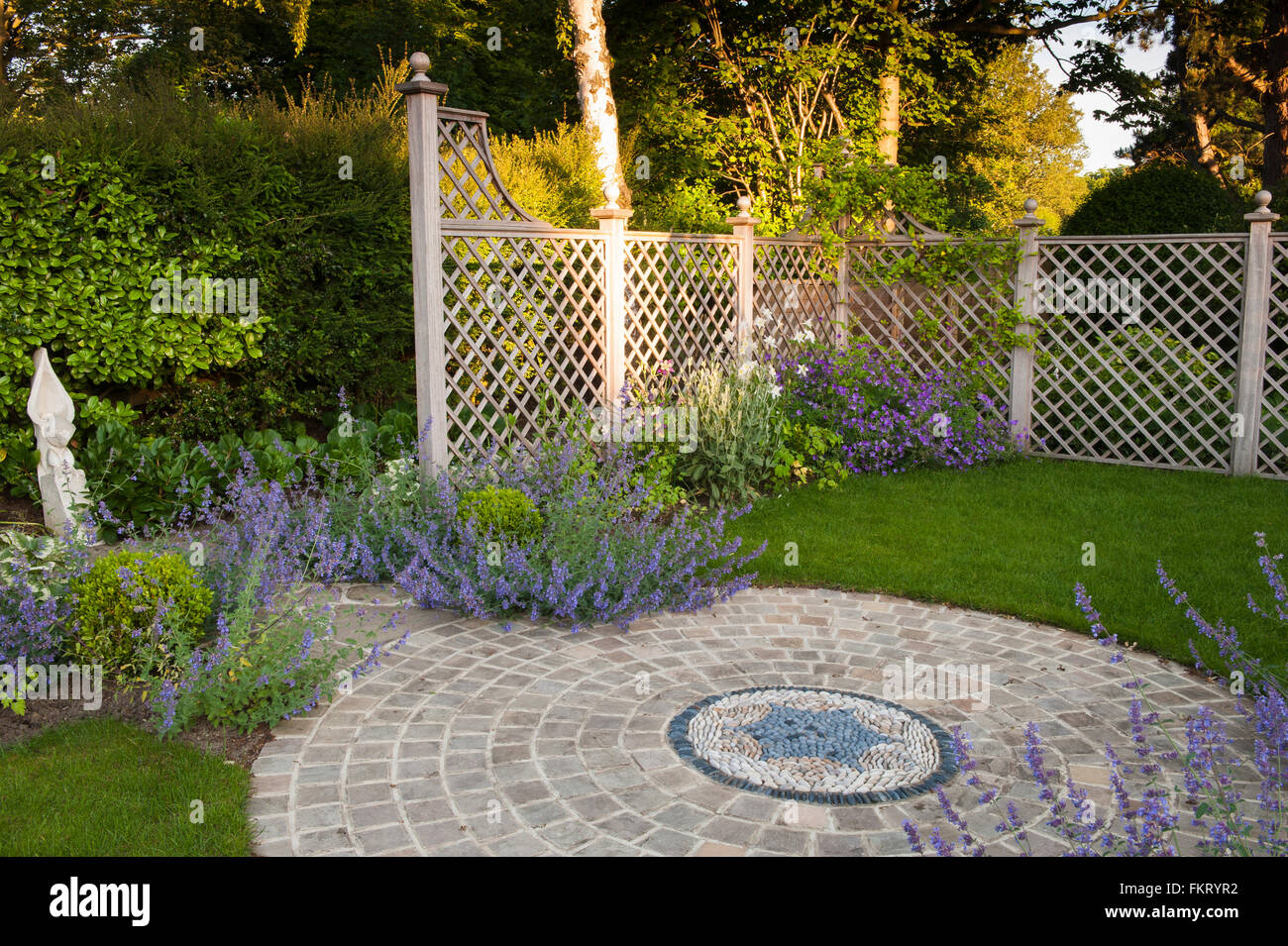 Mosaik, Pflasterarbeiten, blühende Pflanzen, Skulpturen und Rankgitter in sonnigen, gestaltete, gepflegte, Garten, Burley in Wharfedale, Yorkshire, England. Stockfoto