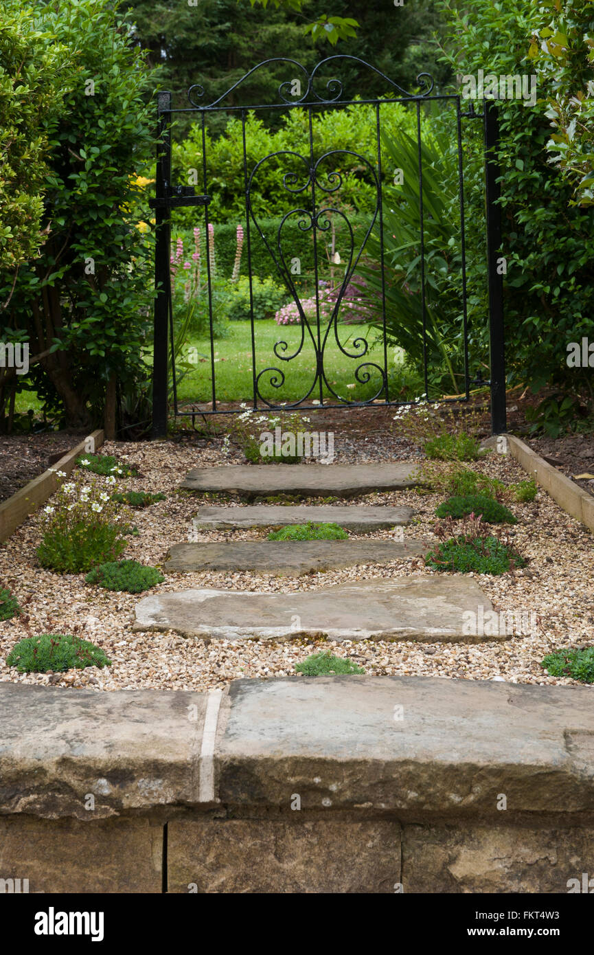 Schmiedeeisernes Tor & rustikal, steinigen Pfad und Stufen, in einem schönen, traditionellen, englischen Garten, Burley in Wharfedale, Yorkshire, England, im Sommer. Stockfoto