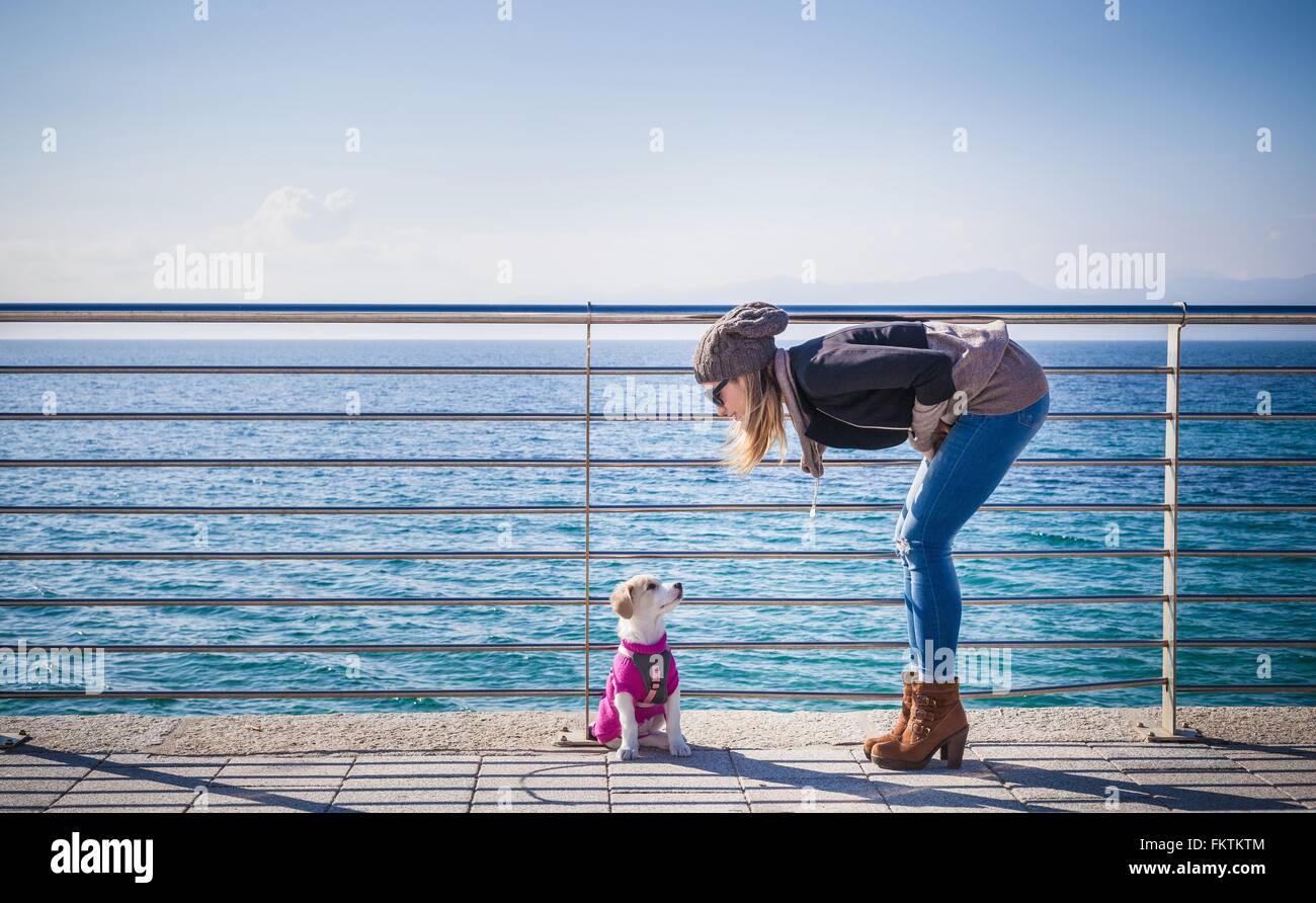 Voller Länge Seite Ansicht junge Frau durch Geländer im vorderen Ozean betrachtet man Hund bücken Stockfoto