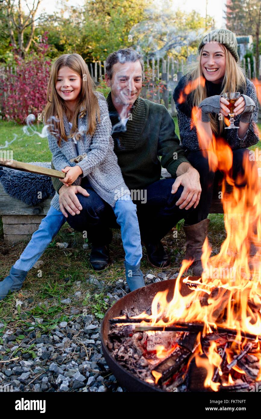 Mädchen mit Mutter und Vater sitzen im Garten mit Feuerstelle Stockfoto