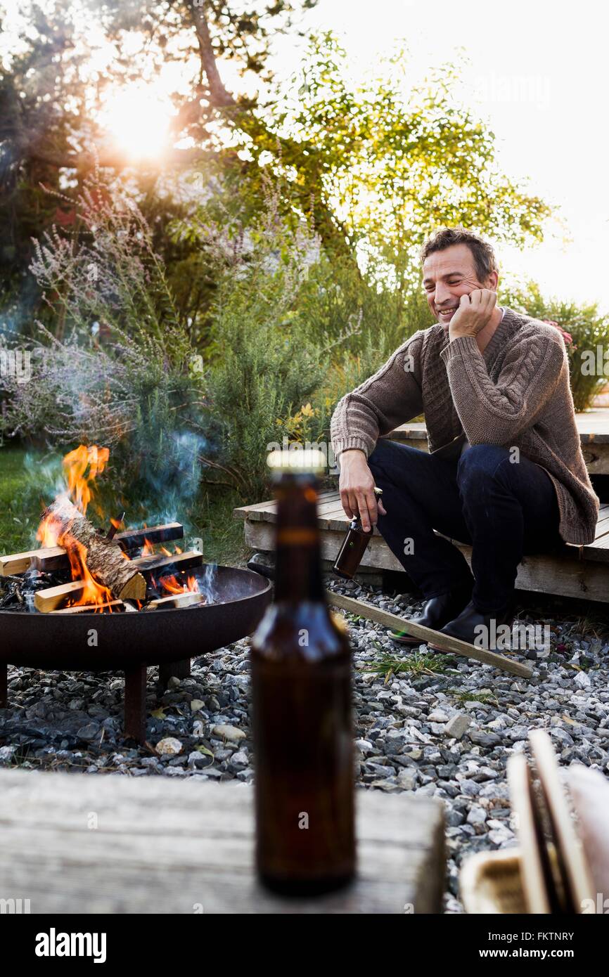 Reifer Mann Feuerstelle mit Bier zu sitzen, relaxen Stockfoto