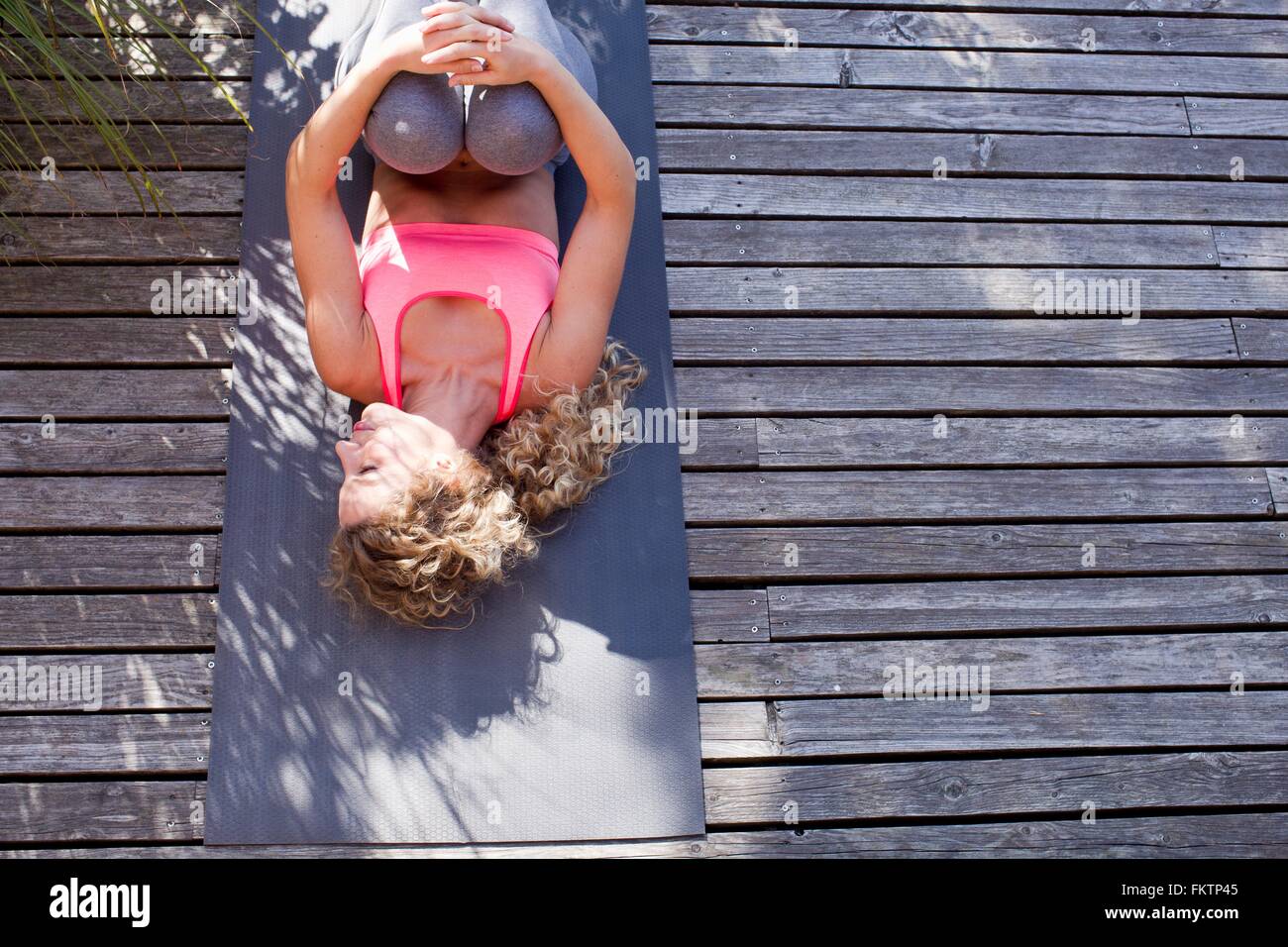 Junge Frau auf Yoga-Matte liegend, Knien, hoher Winkel umarmt Stockfoto